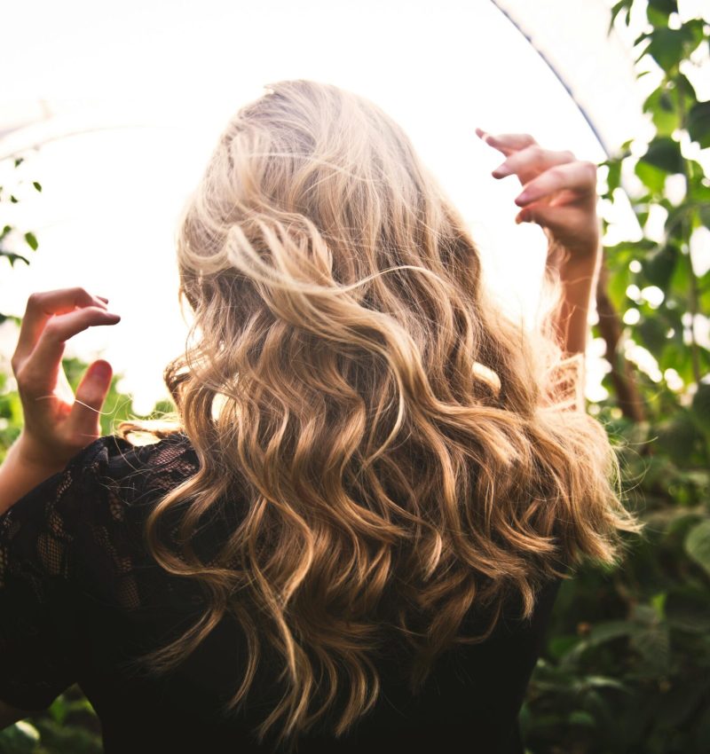 pexels-photo-1049687-1049687 Blonde woman with curly hair surrounded by lush greenery, enjoying a sunny day.